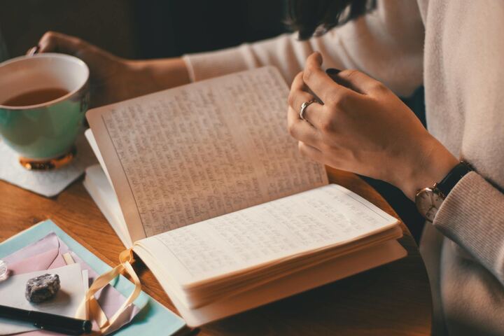 Mãos escrevendo num caderno aberto, com uma xícara de chá ao lado