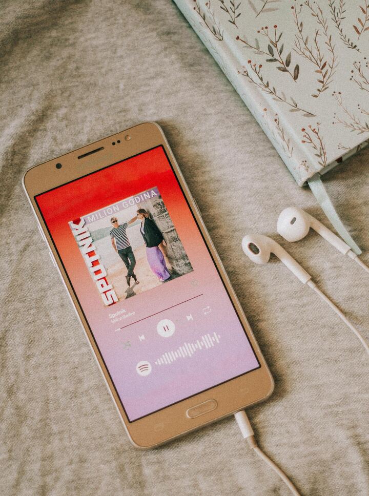 Smartphone tocando música sobre tecido bege com fones e caderno florido